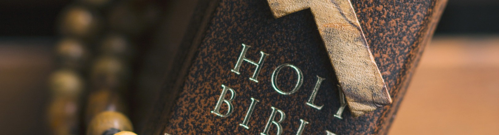 Close-up of a Holy Bible beside a wooden cross