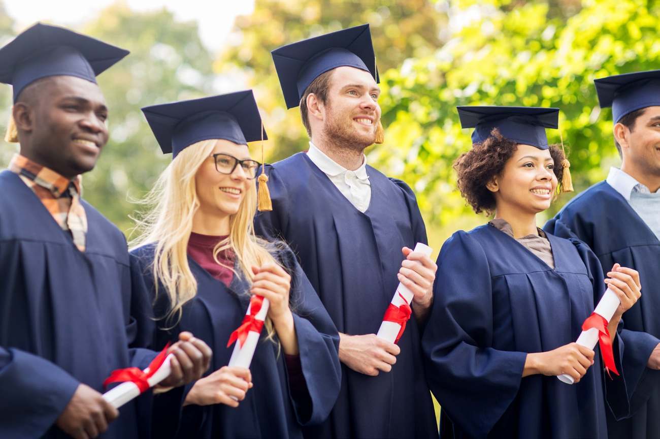 A group wearing graduation gowns and holding rolled certificates outdoors