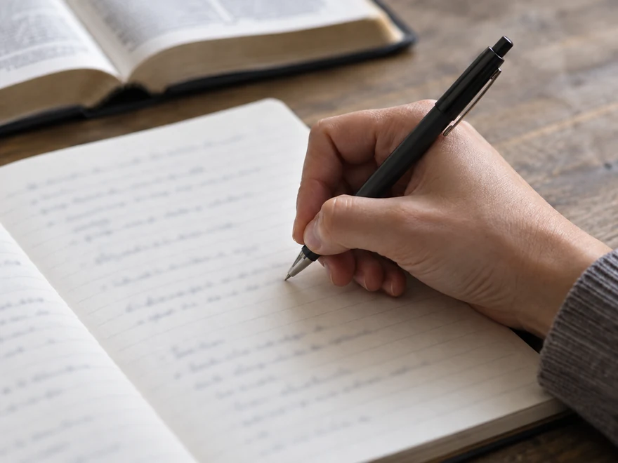 Illustration of a hand writing study notes beside an open book