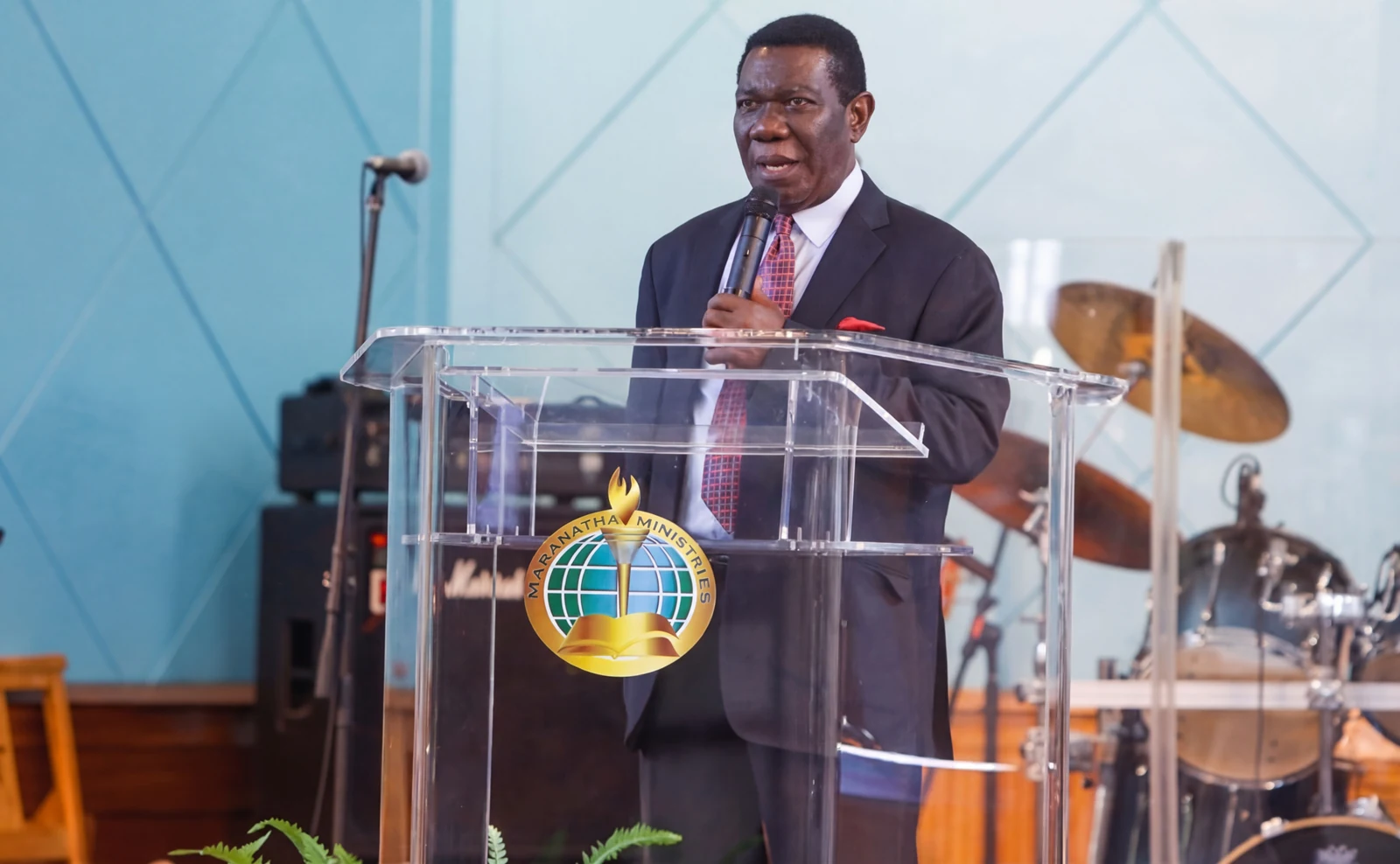 A man speaking into a microphone behind a transparent lectern.